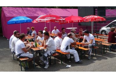 Maifestbesucher auf Festbänke in Sonne unter Sonnenschirmen