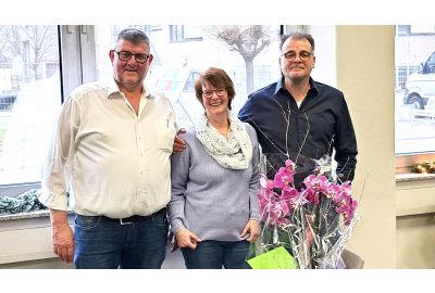 Ralf Winkler, Irmtraut Reinemer (geht in den Ruhestand) und Stefan Winkler mit einer lila Orchidee und einem grünen Umschlag im Vordergrund