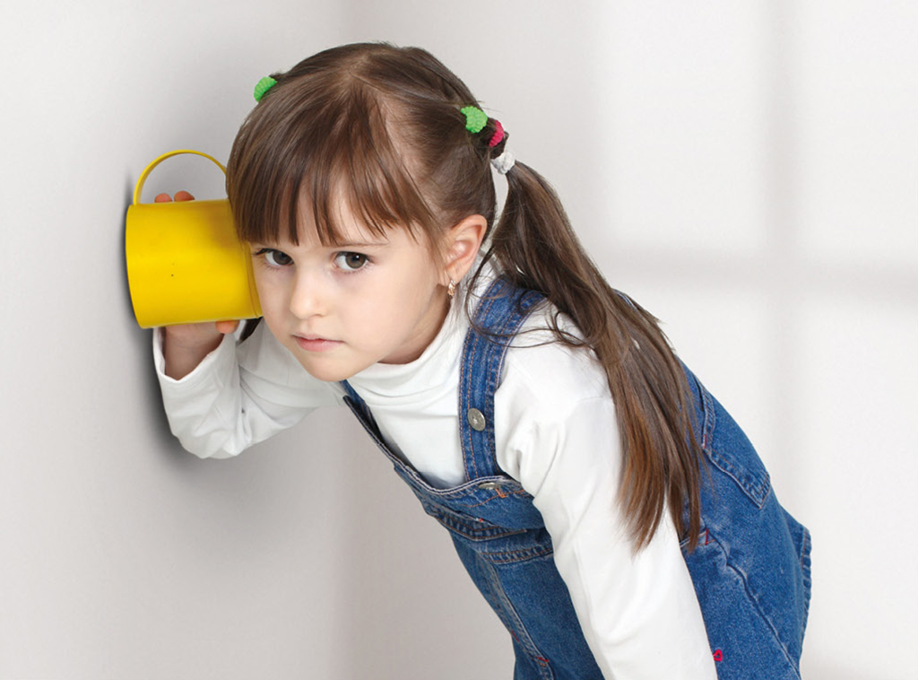 Mädchen lauscht mit einer gelben Tasse an der Wand