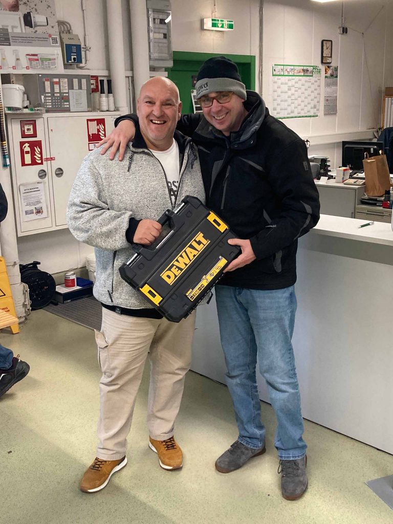 Dennis hat seinen Kunden im Arm - dieser hat einen DeWALT-Koffer in der Hand