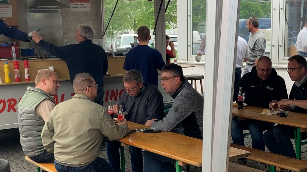 Menschen auf Bierzeltgarnituren beim Essen, Trinken und sich unterhalten
