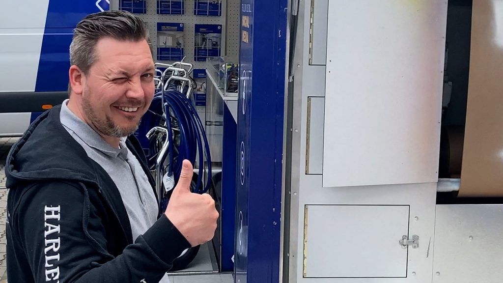 Kunde steht vor dem Spritzstand, zwinkert mit dem Auge und hebt den Daumen nach oben