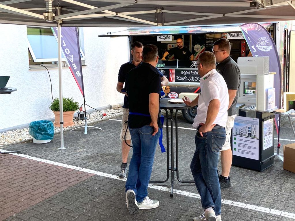 Personen am Stehtisch - im Hintergrund der Pizzawagen