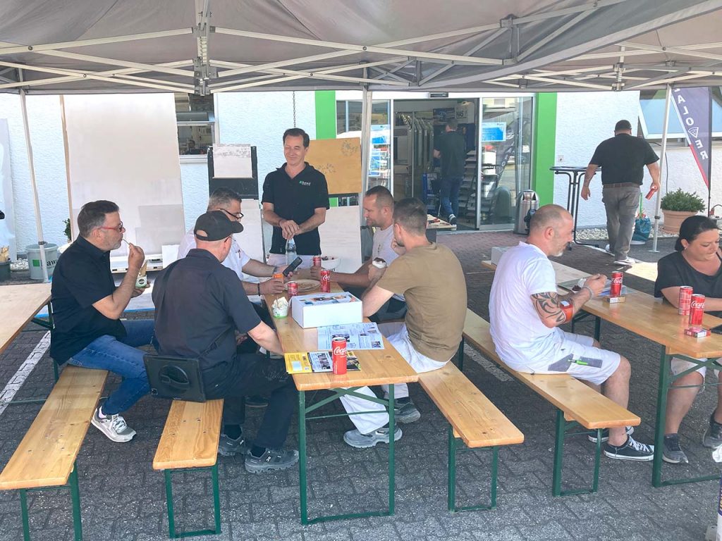 Besucher sitzen im Außenbereich der Filiale Darmstadt auf Bierzeltgarnituren