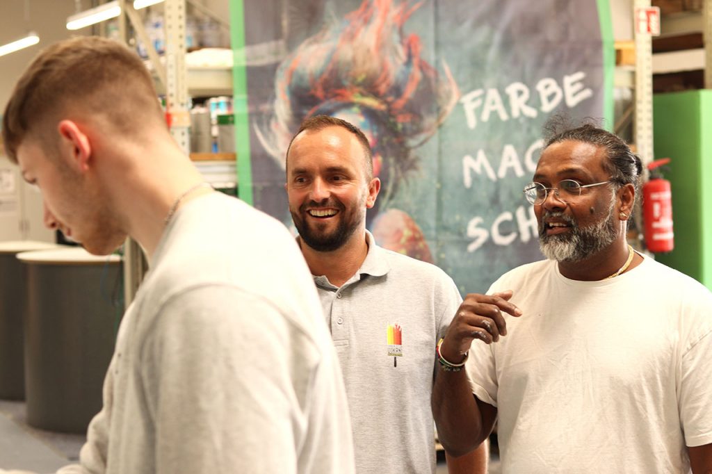 Dilip und Maler Ujkani beobachten jemanden beim erstellen einer Musterplatte