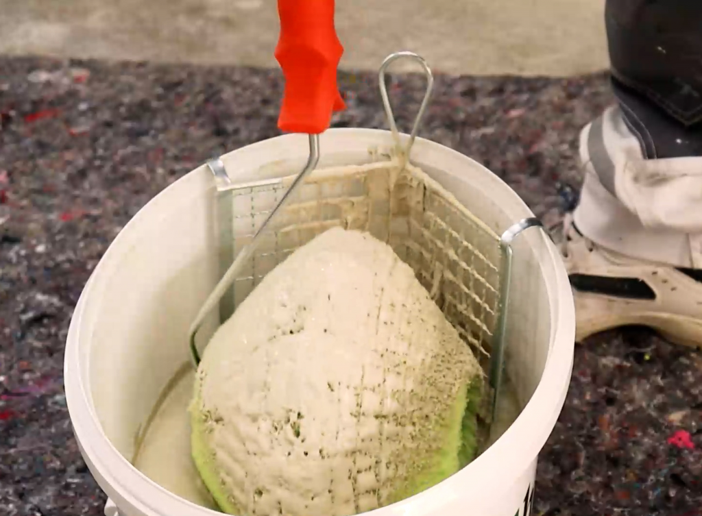 gebogenes Metall-Abstreifgitter aus verzinktem Welldraht im Eimer mit Farbe. Der Eckenroller wird abgerollt, damit er nicht tropft.