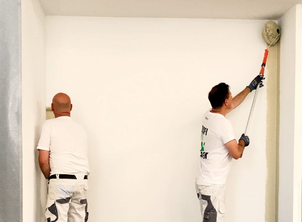 Maler walzt eine Ecke mit dem Maler-Jumbo Eckenroller, der andere in der anderen Ecke mit einer Heizkörperwalze