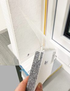 Eine Hand hält ein Muster einer Leibungsplatte mit grauem EPS - im Hintergrund eine Fensterleibung
