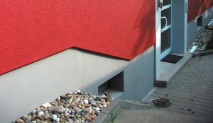 grauer Haussockel eines rot verputzen Hauses.