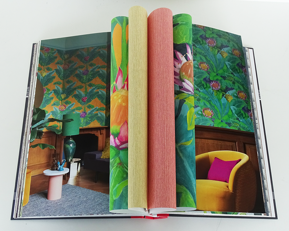 Aufgeklappetes Tapetenbuch mit Raumbildern und farbenfrohen Tapeten